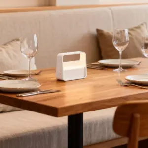 Lámapra de mesa portátil con asa BAG en una mesita auxiliar negra junto a una revista en salón moderno y elegante